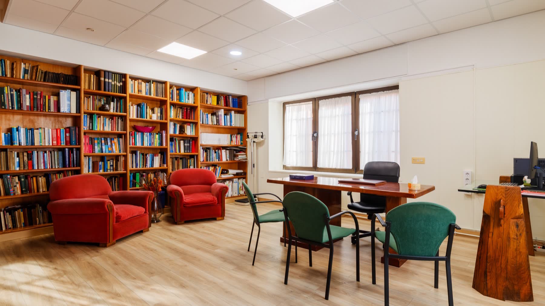 Despacho de consulta con mesa, butacas y una pared entera de estanterías de libros