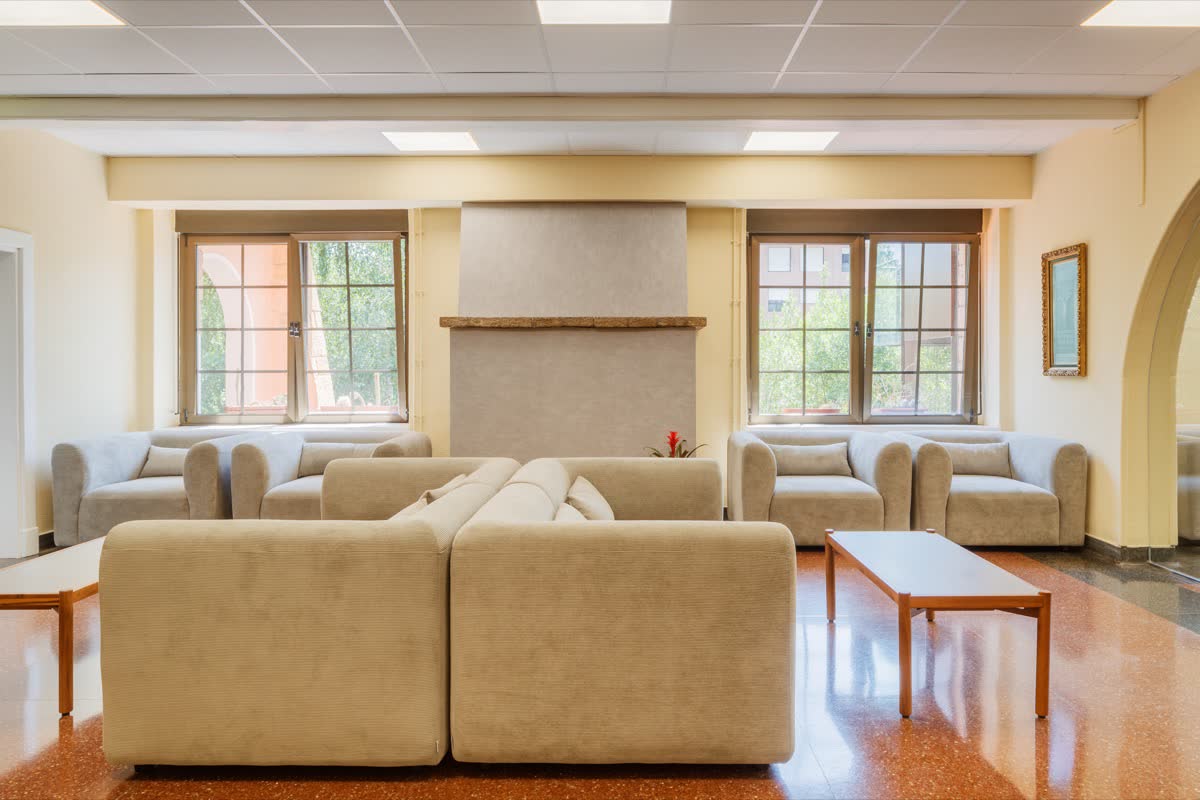 Sala de estar con sofás beige alrededor de una chimenea, entre dos ventanas al jardín