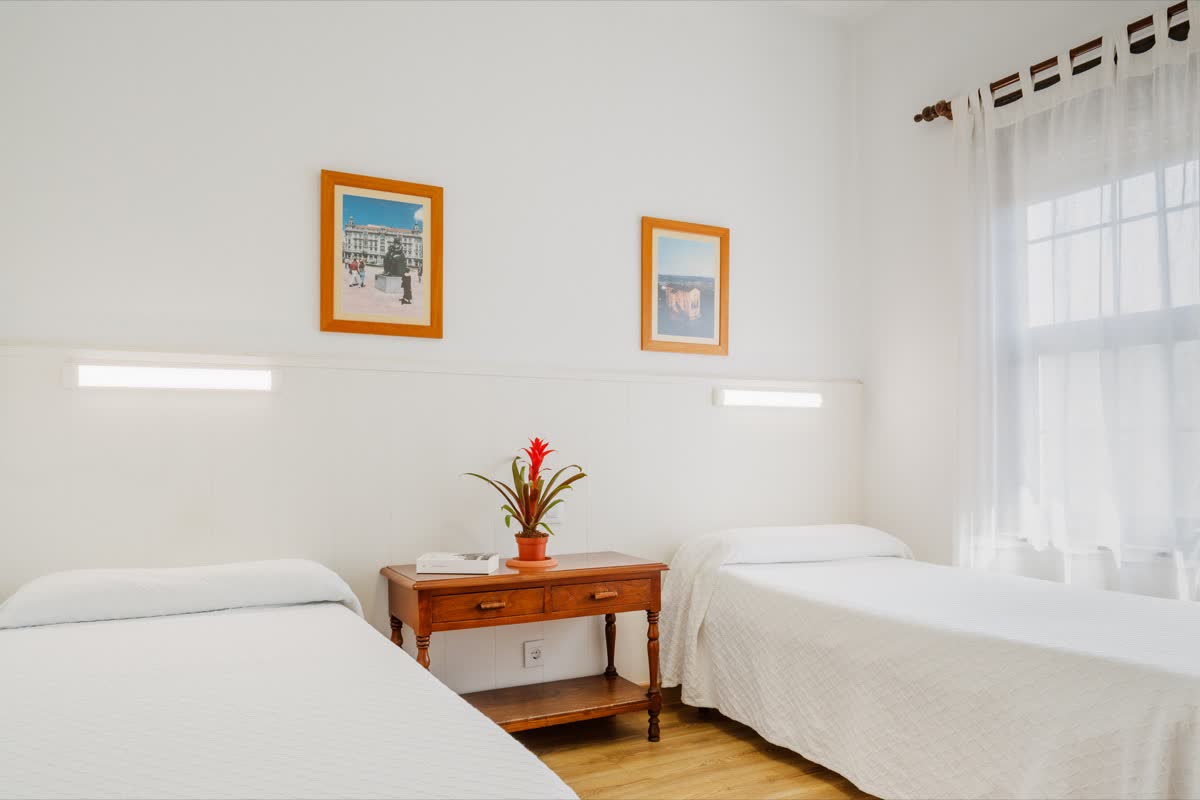 Habitación doble con dos camas, mesilla de madera y ventana con visillos