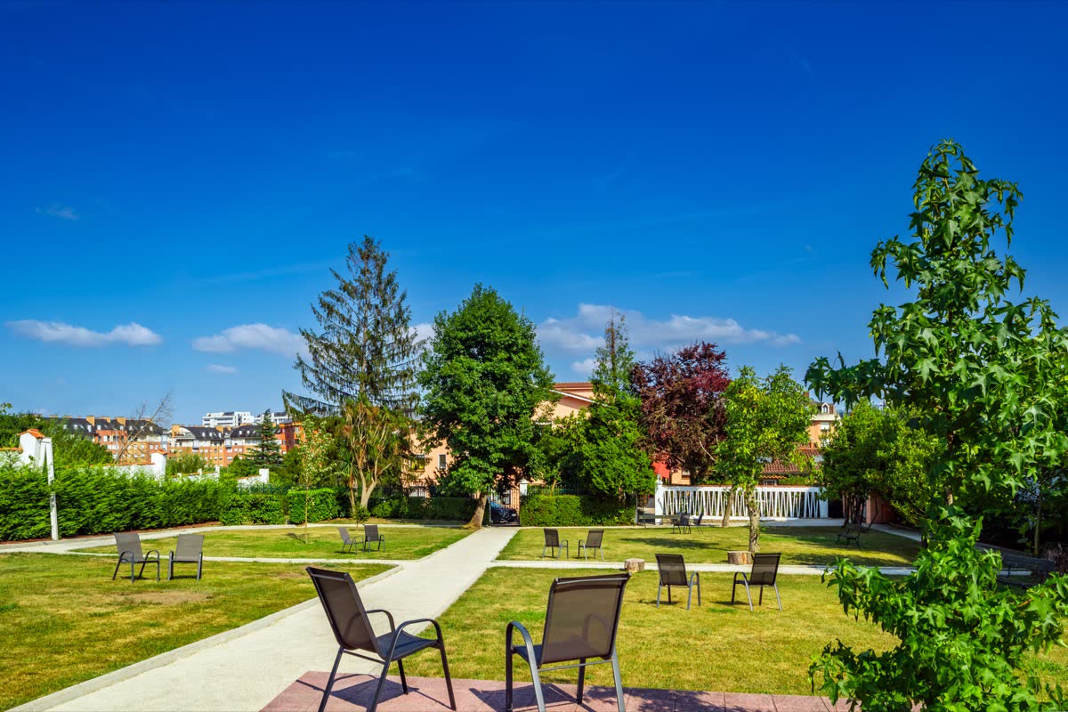 Pradera del jardín con sillas repartidas, paseos de losa y arbolado